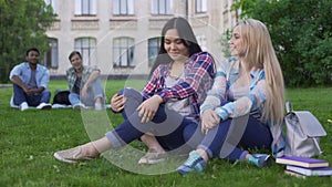 Females sitting on grass, talking and smiling, guys looking at girls, flirt