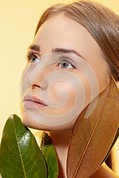 Feminine. Close up of beautiful female face with green leaves over white background. Cosmetics and makeup, natural and