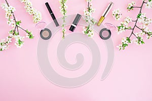 Feminine desk with cosmetic: lipstick, shadows, mascara and white spring flowers on pink background. Flat lay, top view. Beauty co