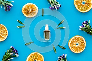 Feminine desk with perfume bottle, flowers and dry oranges on blue background top view pattern