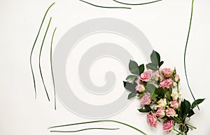 Feminine desk with pink roses, green leaves, and gift bag on white background. Flat lay, top view. Flower background. Women`s day,