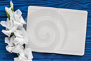 Feminine desk workspace. Notebook and gladiolus on blue wooden background top view mockup