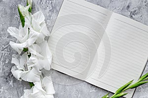 Feminine desk workspace. Notebook and gladiolus on grey stone background top view mockup