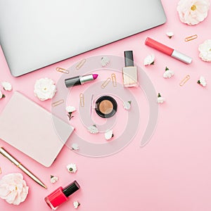 Feminine desktop with laptop, notebook, cosmetics and flowers on pink background. Top view. Flat lay lifestyle concept.