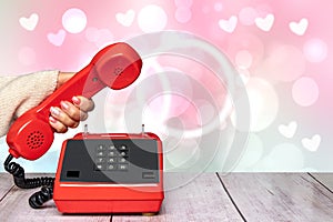 A feminine elegant beautifully manicured woman`s hand holding an old red telephone handset over an abstract blurry light pink