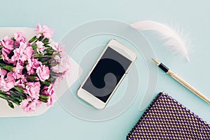 Feminine flat lay on blue background, top view of woman`s desktop with envelope, flowers, pen, notepad and smartpho