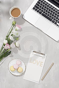 Feminine flat lay workspace with laptop, cup of tea, macarons, Love letter and flowers on white table. Top view mock up