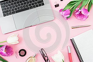 Feminine office desk with laptop, tulip flowers, cosmetics, glasses and pen on pink background. Flat lay. Top view. Concept with c