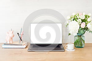 Feminine office desk table with laptop computer with blank white screen, bouquet of flowers, unicorn, stationery and supplies.