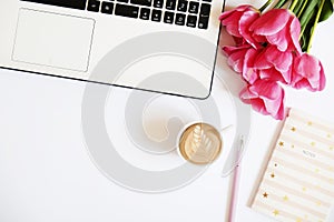 Top view of female worker desktop with laptop, flowers and different office supplies items. Feminine creative design workspace.