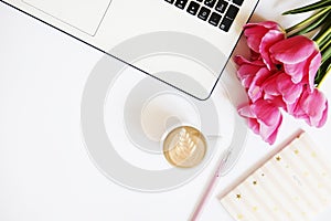 Top view of female worker desktop with laptop, flowers and different office supplies items. Feminine creative design workspace.