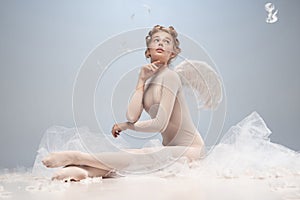 Portrait of pretty, slim beautiful young girl, graceful ballerina in image of angel with wings sitting on cloud