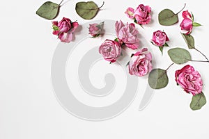 Feminine wedding desktop composition with pink roses flowers, dry green eucalyptus leaves isolated on white table