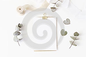 Feminine wedding desktop stationery mockup with blank greeting card, dry eucalyptus leaves, silk ribbon and golden