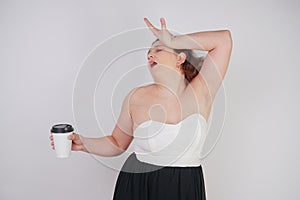 Feminine woman with plus size body in a fashionable dress holding a paper Cup of coffee and posing on a white background in the St