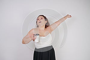 Feminine woman with plus size body in a fashionable dress holding a paper Cup of coffee and posing on a white background in the St