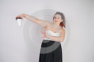 Feminine woman with plus size body in a fashionable dress holding a paper Cup of coffee and posing on a white background in the St