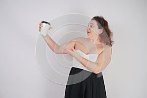 Feminine woman with plus size body in a fashionable dress holding a paper Cup of coffee and posing on a white background in the St