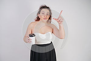 Feminine woman with plus size body in a fashionable dress holding a paper Cup of coffee and posing on a white background in the St
