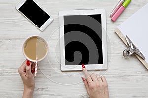 Feminine work space with tablet, noticepad, sheet, latte ice, smartphone and female hands over white wooden background, top view.