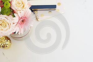 Feminine workplace concept in flat lay style with, flowers, golden pineapple, notebooks on white marble background. Top view, brig