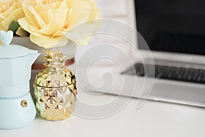 Feminine workplace concept. Freelance workspace with laptop, flowers, golden pineapple. Blogger working. Bright, yellow and gold.