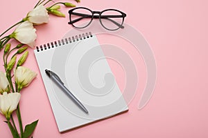 Feminine workplace with jotter, eyeglasses and flowers in pastel