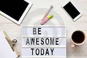 Feminine workplace with tablet, noticepad, sheet, coffee and `Be awesome today` words on light box over white wooden desk, top v