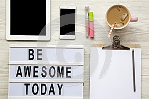 Feminine workplace with tablet, noticepad, sheet, latte ice and `Be awesome today` words on lightbox over white wooden surface,