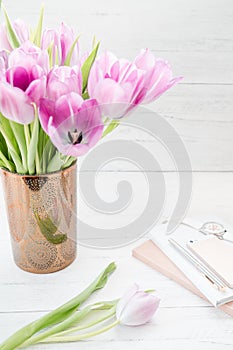 Feminine workspace. Bright and airy desk top with notepad and pink tulips. Vertical