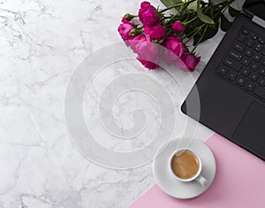 Feminine workspace with laptop computer, bouquet of roses and coffee on a marble table.