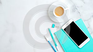 Feminine workspace with mint paper notebook, cup of coffee, office supplies, smartphone on marble desk. Flat lay, top view, copy