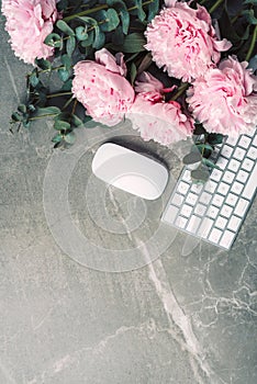 Feminine workspace. White computer keyboard, mouse, peony flowers, eucalyptus flowers on marble background. Top view. Copy space.