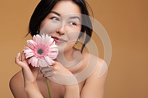 Feminine young Asian lady with fresh flower in hand smiling in studio