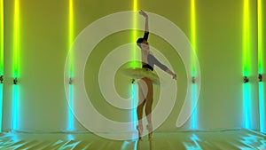 A feminine young graceful ballerina is dancing elements of classical ballet in the studio against a background of bright