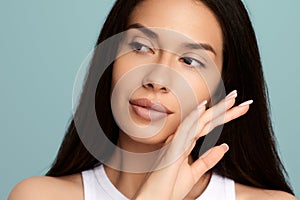 Feminine young woman with natural makeup touching face in studio