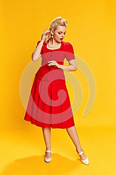 Femininity. Portrait of beautiful young blonde woman with stylish hairstyle in red suit posing against yellow studio