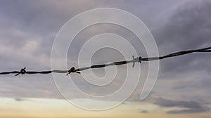 Fence of barbed wire on the beach against the background of beautiful sunrise.