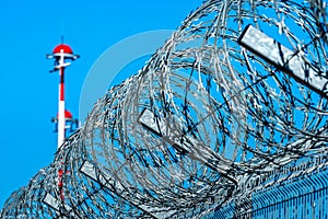 Fence with barbed wire and row of the airport lamp posts with alternate red and white painting against blue sky