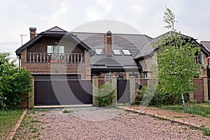 Fence and brown gate of metal overgrown with green plants in front of a private house