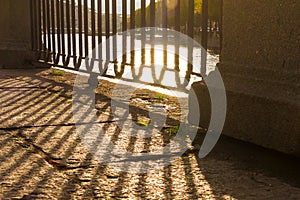 Fence of embankment and its shadow on pavement closeup