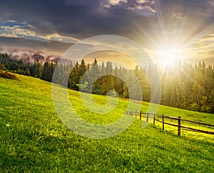 Fence on hillside meadow in mountain at sunset