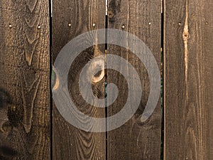 The fence is made of brown-painted wooden boards with defects