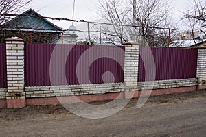 Fence made of red metal and gray brick on a rural street
