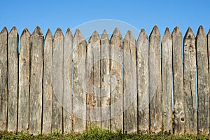 Fence made of sharp wooden stakes against the blue sky. Wooden fence vertical logs pointed against the sky protection against inva