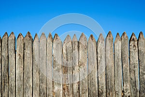 Fence made of sharp wooden stakes against the blue sky. Wooden fence vertical logs pointed against the sky protection against inva