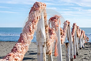 A fence made of wooden logs and rope rope in the sand on the dock on the beach promenade near the sea in Italy