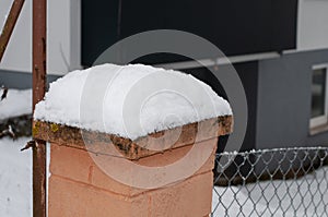 A fence post with snow at a metal fence