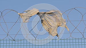 Fence prison strict regime. piece of torn clothing fugitive hanging on barbed wire on a windy day. concept illegal immigration ref