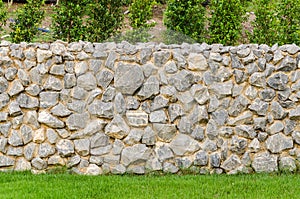 Fence real stone wall surface with cement on green grass field